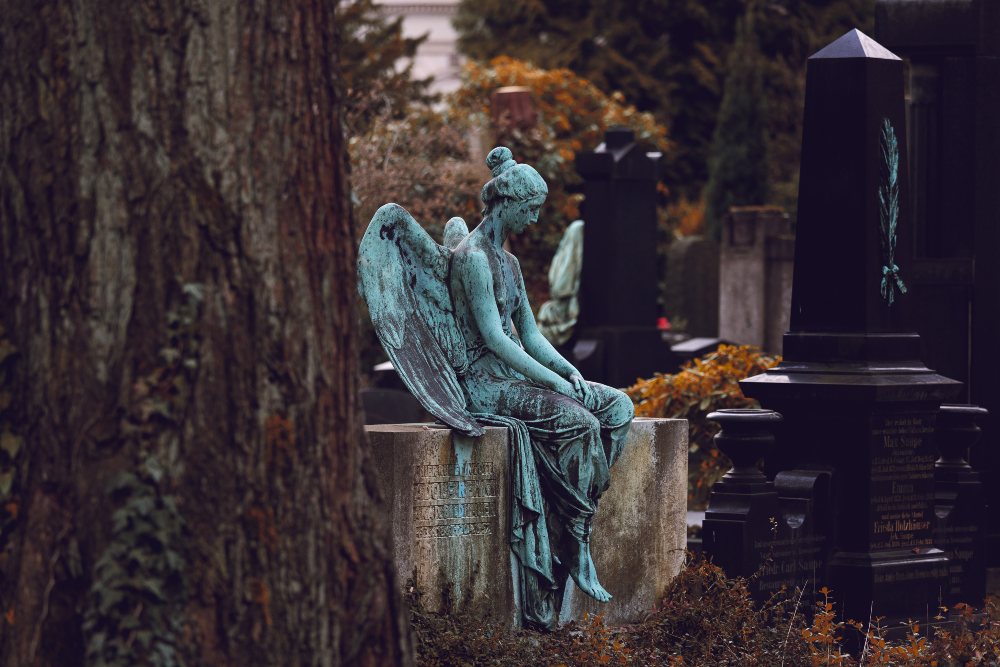 A blue statue of an angel sits in a cemetary.