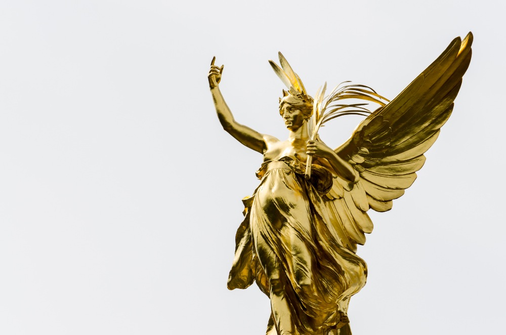 A golden angel statue up against a white backdrop.