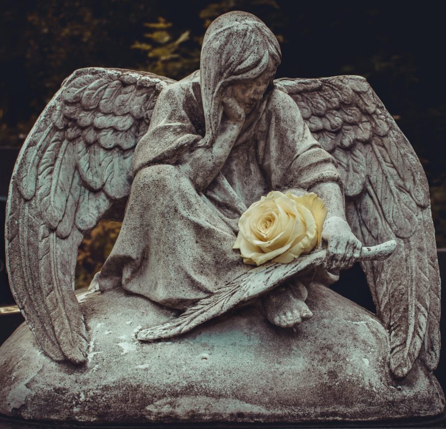 A statue of an angel holding a yellow rose as she sits.