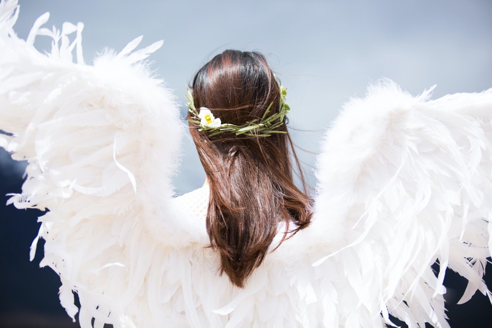 The back of a woman wearing angel wings. She has long dark brown hair.